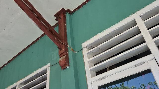 Low angle shot of white wooden louver windows and structural support beam against a turquoise green wal