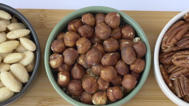 Camera slowly travels across bowls of almonds, hazelnuts and pecans revealing healthy fats and vitamin E rich nuts that support heart health and nutrition.