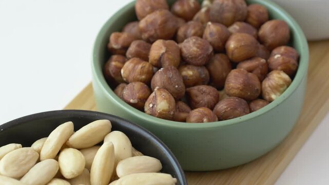 Slow camera movement passes over bowls of almonds, hazelnuts and pecans showing a combined source of plant protein, magnesium and zinc for daily nutrition. Balanced healthy eating habits.