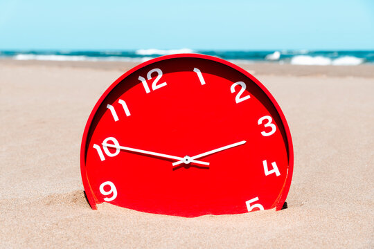 a close-up of a red clock half buried in the sand