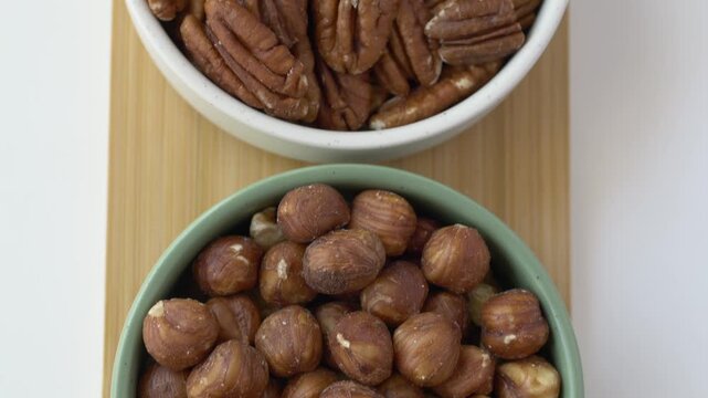 Top down view of assorted nuts arranged in bowls. Footage emphasizes natural plant based nutrition, healthy fats, protein and dietary fiber while showcasing a variety of nutrient rich snack options.