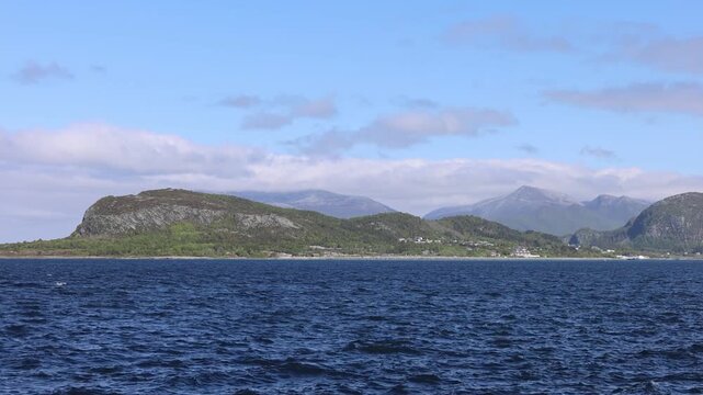 View of the rugged coastal mountains and deep blue sea under a blue sky in Alesund, More og Romsdal, Norway.