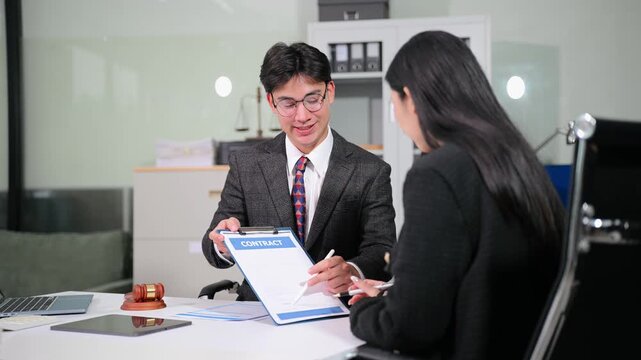 Professional Asian attorney explains legal contract terms to a businesswoman, leading to a successful deal and handshake in a modern law office workspace.