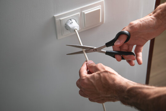 Man with a scissors cutting of electrical plug.