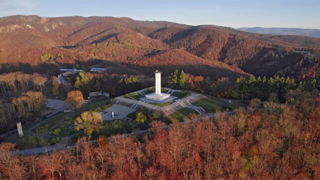 Aerial view of the SNP World War II memorial on Jankov Vrsok surrounded by autumn forest and rolling hills in warm evening light, Uhrovec, Slovakia