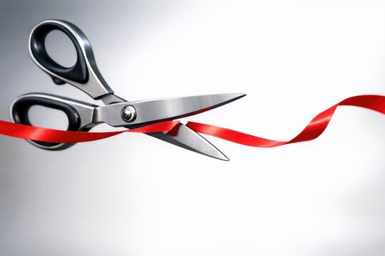 A pair of scissors cutting through a bright red ribbon, ideal for use in graduation, achievement, or celebration scenes