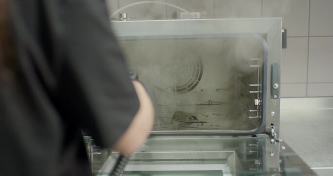 Close up view of worker scrubbing oven interior back panel with a high pressure steam wire brush