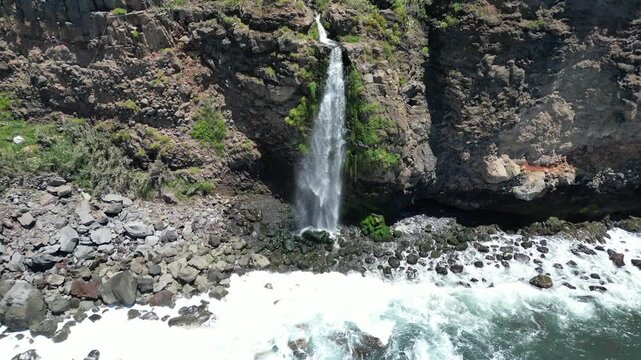 Aerial view of Cascata do Mito waterfall crashing into ocean Madeira