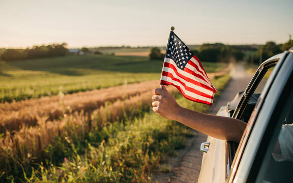 Person holding an american flag out of a car window while driving through scenic rural countryside during golden hour transparent background