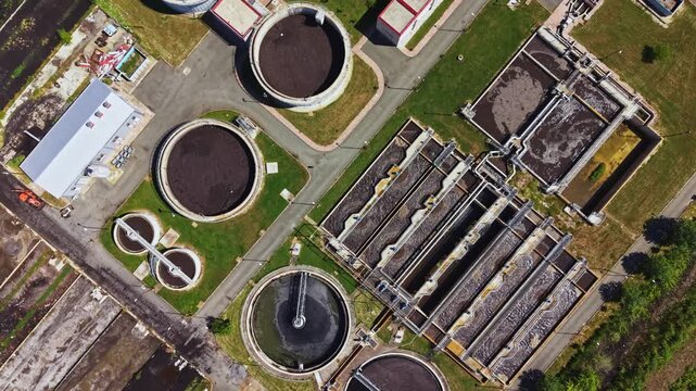 Aerial view sewage treatment plant tanks showing circular clarifiers, aeration basins, sludge processing lanes, access roads, green buffers, facility buildings