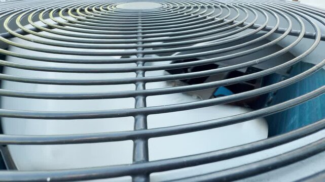 An air conditioner fan stops completely inside an outdoor cooling unit. The powerful machinery shuts off entirely, leaving only the quiet clicking silence of a final industrial shutdown sound.