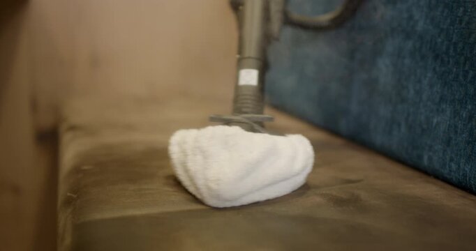 Close up view of steam tool extension moving across and cleaning brown velvet restaurant booth cushion
