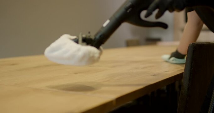 Worker in black safety gloves using a white pad extension tool to clean a modern wooden conference table