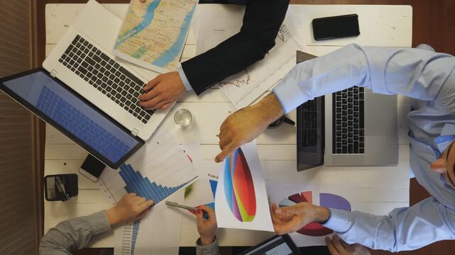Top view to male and female hands of managers examining financial graphs at office. Group of entrepreneurs create corporate project sitting at table. Young coworkers working on business development