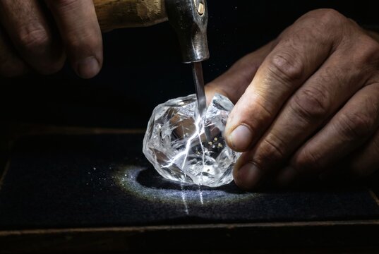 Master Diamond Cutter Hands Cleaving Large Raw Diamond with Chisel and Hammer on Dark Velvet Surface with Light Flash and Diamond Dust