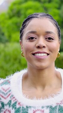 Vertical video: Smiling woman reacting to offscreen joke, turning, laughing in park, fuzzy sweater
