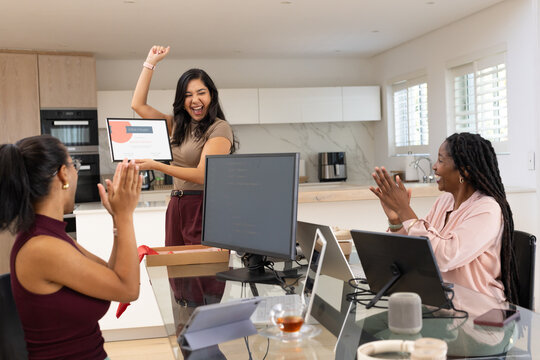 Diverse female team in office wear clapping, colleague holding framed certificate at kitchen office