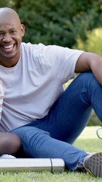 Vertical video: Camera zooming, dad and son leaning, bonding on blanket in park, holding mug, flask