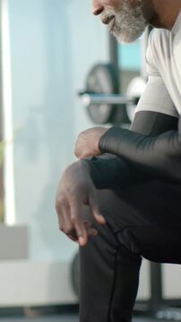 Vertical video: Resting mature man in gym top breathing after set at bench, weight plates behind
