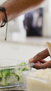 Vertical video: Right hand reaching, scooping broccoli into box in kitchen, for lunch, yellow shirt