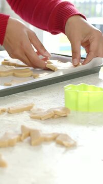 Vertical video: Picking up cutouts, red-sweater hands arranging for baking on tray, green cutter