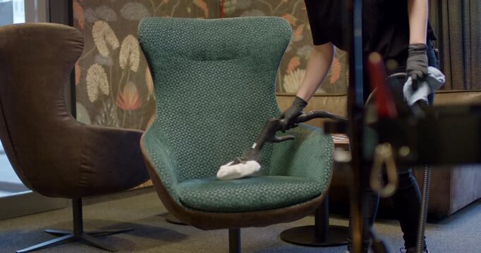Worker using professional steam tool extension nozzle with white pad to deep clean fabric armchair