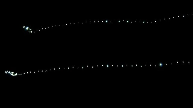 Rows of glowing white string fairy lights hanging against a completely dark black night background