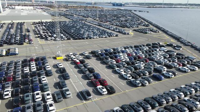 Sideways drone flight crosses endless cars toward the port edge and sea.