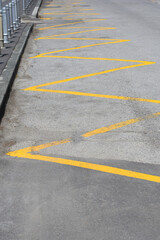Obraz premium Yellow zig zag lines are painted on the grey asphalt road next to a pavement curb marking a no parking zone or bus stop