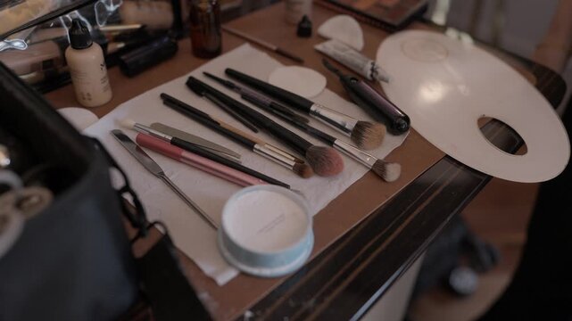 Collection of makeup brushes pencils foundation and palette arranged on wooden dressing table surface