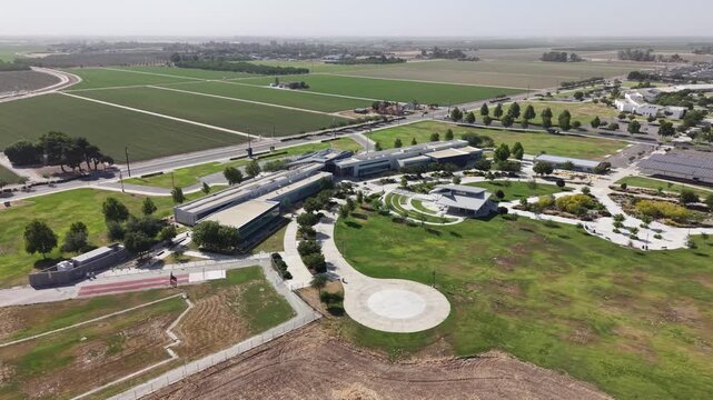 Panning drone perspective showing the modern architecture of the College of the Sequoias campus, situated amidst the lush green farmlands and rural landscape of Visalia, California on a sunny day
