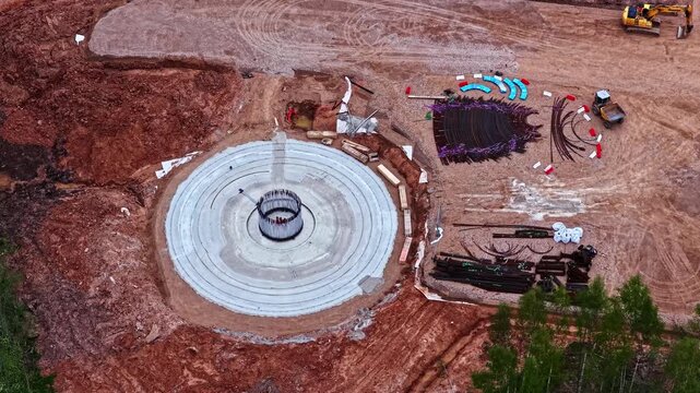 Workers building wind turbine foundation with rebars at a large construction site, aerial view