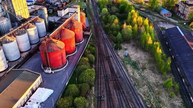 Llarge industrial grain elevators and railroad tracks at sunset in aerial view