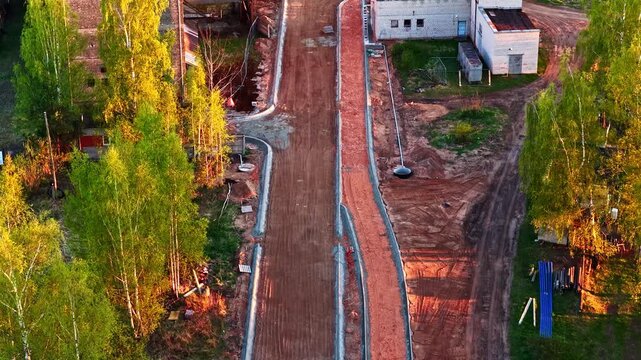 Road construction with sidewalk and bicycle path in a park at sunset in aerial view