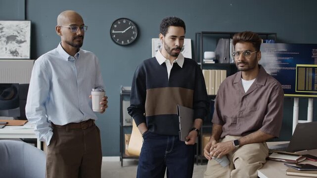Zoom in slowmo portrait of multiethnic young male IT specialists standing in office, holding laptop and coffee, then smiling at camera. Perfect for tech recruitment and corporate website marketing