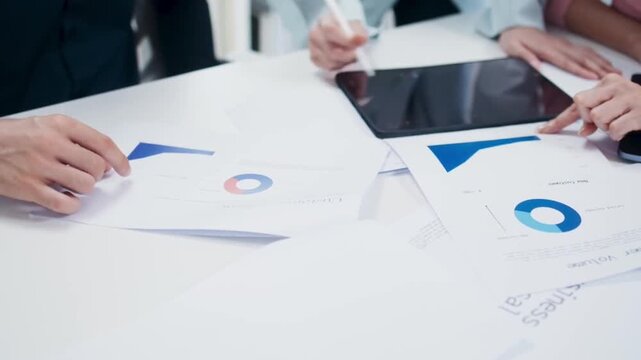 Hands of business professionals analyzing statistical data charts and financial reports on a white desk in a modern office