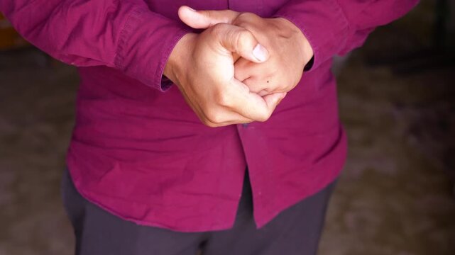 Person clasping hands together a man wearing a maroon shirt his in front of his torso, captured in close up shot