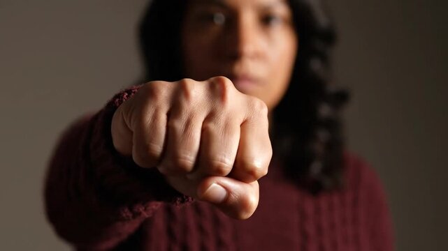 Woman holding a clenched fist toward the camera in a defensive or aggressive pose