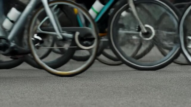 Close low-angle middle sequence of multiple bicycle wheels spinning in road race peloton at peak