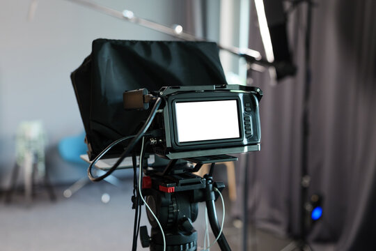 Video camera with white display in studio. Blank screen template of a professional video shoot. Indoors media production for a video podcast for social media content. Behind the scenes perspective.