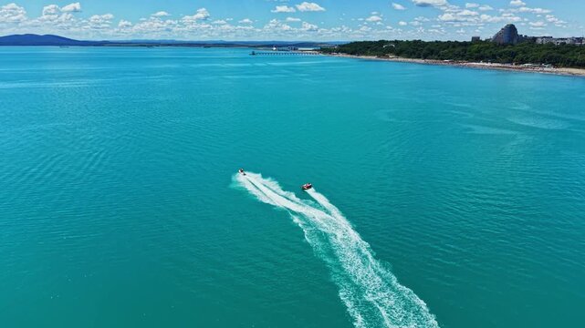 A boat travels swiftly through the turquoise water away from the beach and pier. The sky is bright and clear, making it a nice day for being on the water.