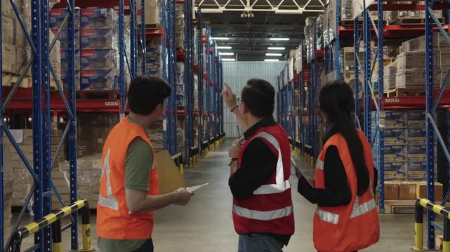 Three workers conduct thorough warehouse inspection utilizing high-visibility vests amidst vast storage facility filled with shelving units and numerous boxes for quality control.