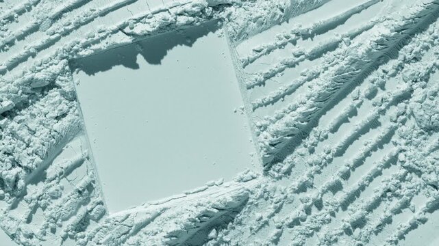 Top perspective capture of powder furrows surface pale cyan natural powder surface with intersected furrows and square imprint illuminated by orbiting directional light that creates shifting shadows