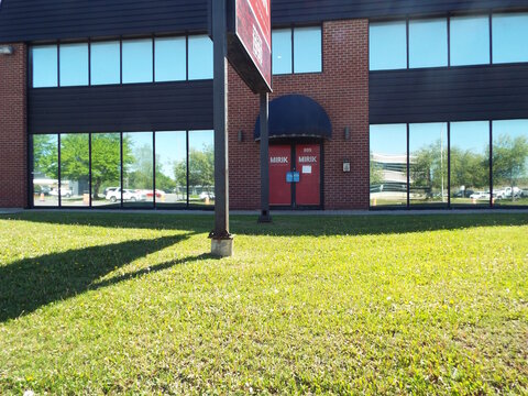 Gatineau,Quebec, Canada &ndash; May 16, 2026: A brick commercial building with large windows and a red door labeled "Mirik" stands behind a grassy lawn at 895 Bd de la Carri&egrave;re.