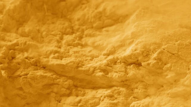 Slow-motion macro shot of split yellow powder surface being blown with a strong air stream, breaking its structure and chipping it into small pieces