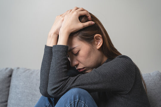 Depressed and stressed young Asian woman sitting on sofa at home.