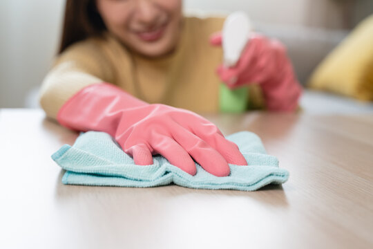 Close up of woman in pink rubber gloves wiping wooden table with microfiber cloth.