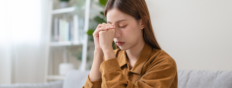 Stressed and depressed young Asian woman sitting on sofa at home, panoramic banner.