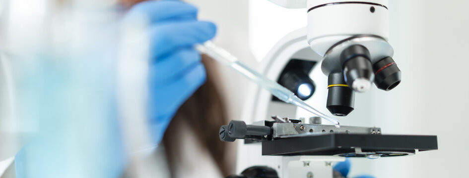 Scientist dropping liquid sample on microscope slide in laboratory, panoramic banner.