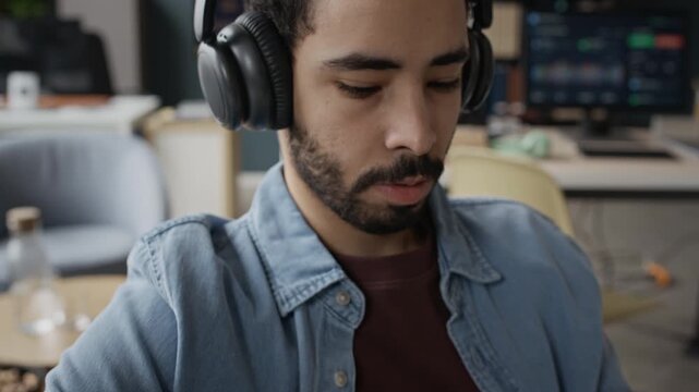 Tilt up shot of young Middle Eastern man wearing headphones typing on keyboard in IT office. Footage is ideal for software development, programming, or online customer support promotions